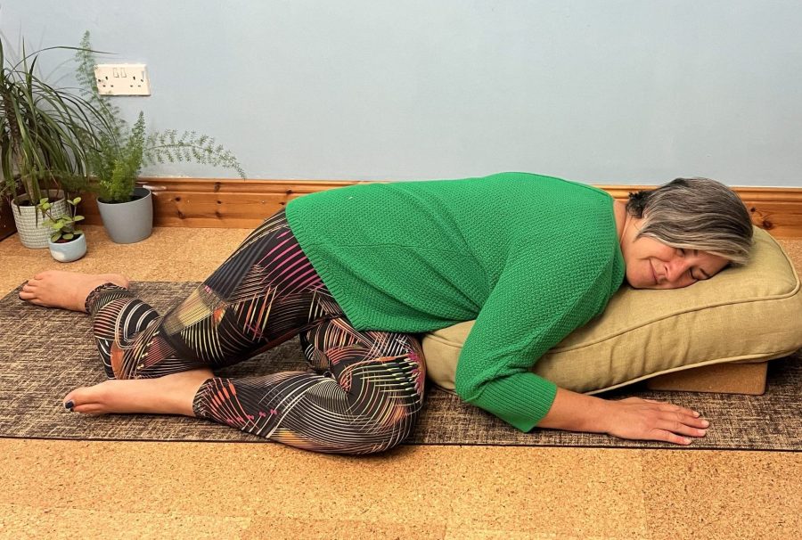 Woman in green jumper lies in a restorative twist on a cushion on a yoga mat
